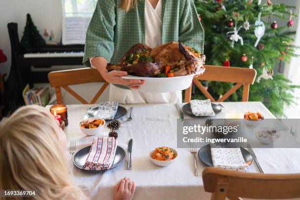woman putting roast turkey on table with daughter at the background - stuffed turkey stock pictures, royalty-free photos & images