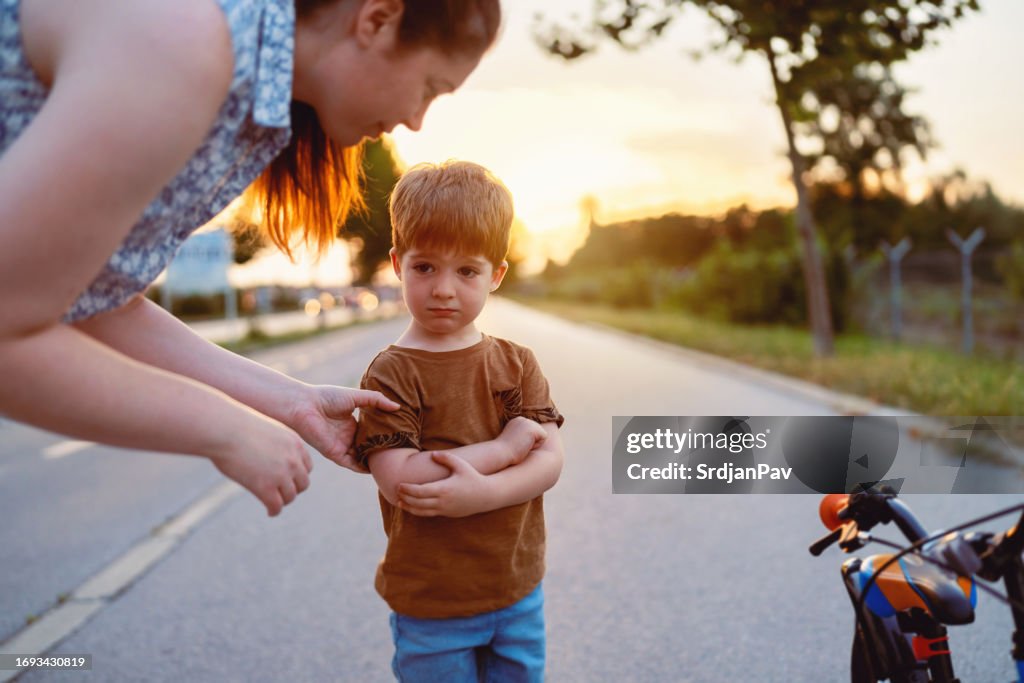 Madre ayudando a su hijo pequeño después de caerse de una bicicleta