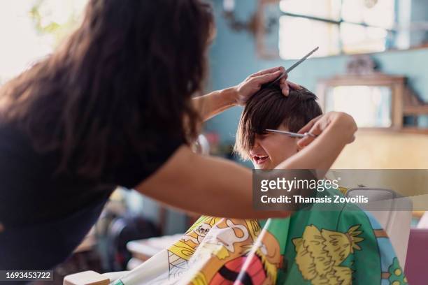 a pretty boy happy to be on the haircut with a professional children's hairdresser. - thanasis zovoilis stock pictures, royalty-free photos & images