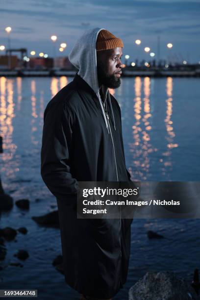 solitude: african american man standing alone near a canal at night - film noir stil stockfoto's en -beelden