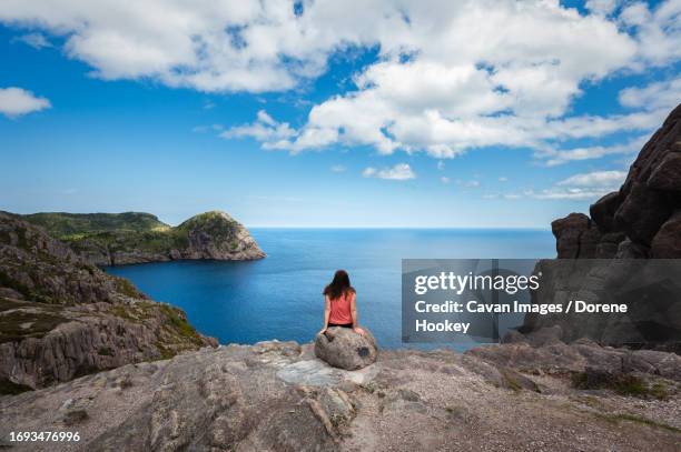 woman sitting on rock overlooking ocean in st. john's, newfoundland - st johns newfoundland people stock pictures, royalty-free photos & images