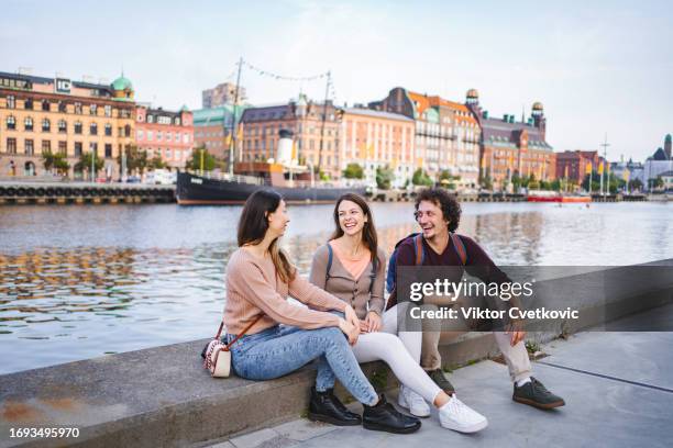 three happy tourists sitting by the river and talking - malmo stock pictures, royalty-free photos & images