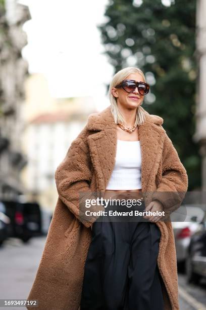 Caroline Daur wears sunglasses, a white crop top, a brown long fluffy winter coat, black wide-leg flared pants, outside Max Mara, during the Milan...