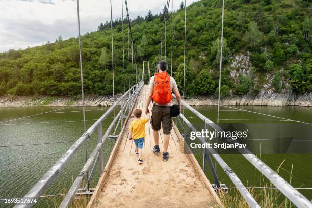 father and son on an adventure, crossing a suspension bridge over the uvac river. - crossed stock pictures, royalty-free photos & images