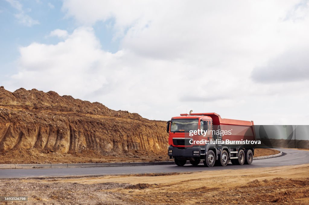 Robust red dump truck rides on asphalt road delivering essential construction materials
