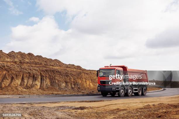 robust red dump truck rides on asphalt road delivering essential construction materials - camión-de-descarga fotografías e imágenes de stock