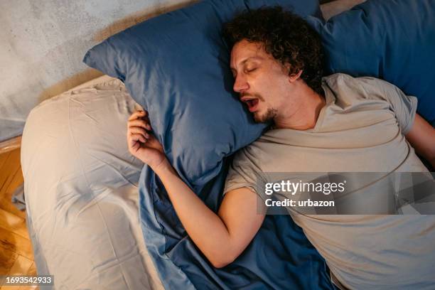 young man snoring in the bed at night - sleep apnea stock pictures, royalty-free photos & images