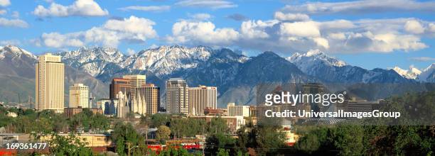 Panorama photo of the Salt Lake City Utah skyline showing downtown buildings and the snow-covered Wasatch Mountains in the background.