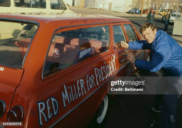 Red Miller , head coach of the Denver Broncos, autographs a car with the slogan 'Red Miller for President' on it, Denver, Colorado, January 6th 1978....