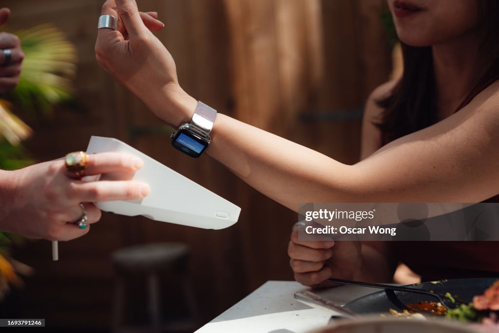 Young woman making contactless payment with smart watch at cafe