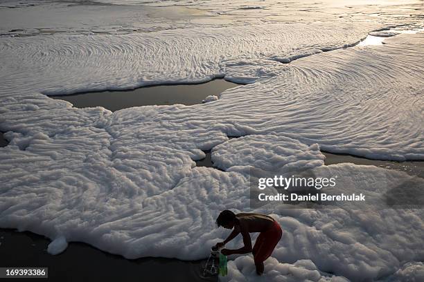 An Indian man collects water as he bathes in an industrial waste-foam polluted section of the Yamuna River, on the outskirts of New Delhi on May 24,...