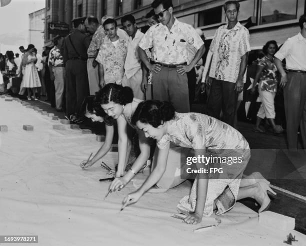 Three Hawaiian women kneeling as they sign Hawaii's Statehood honor roll petition to Congress, which stretches down Bishop Street in Honolulu, on the...