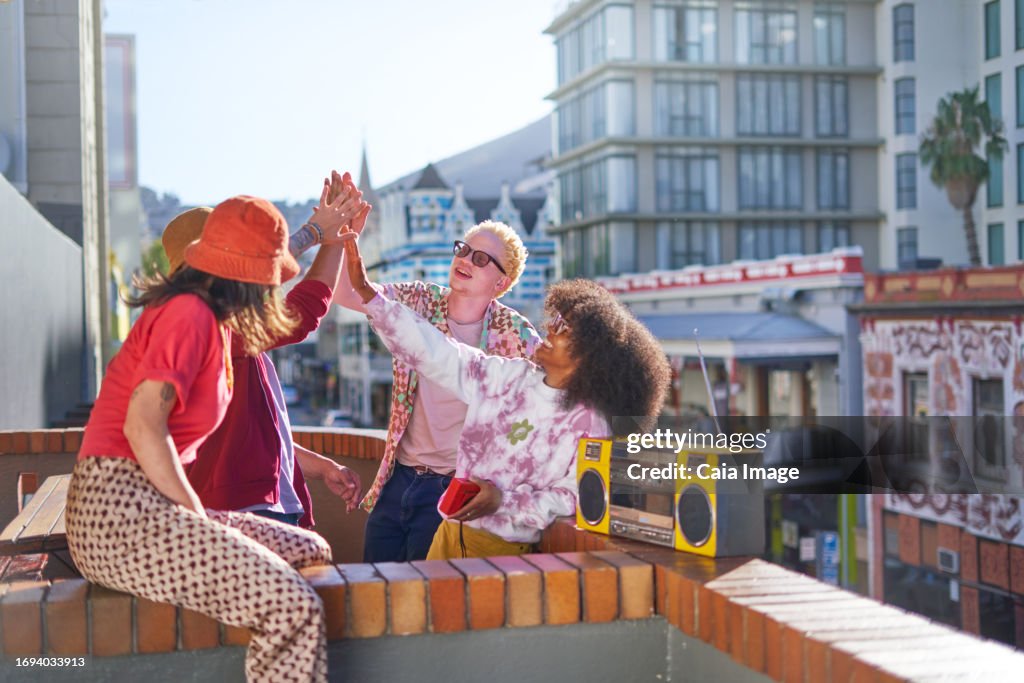 Happy young friends high-fiving on sunny urban city balcony