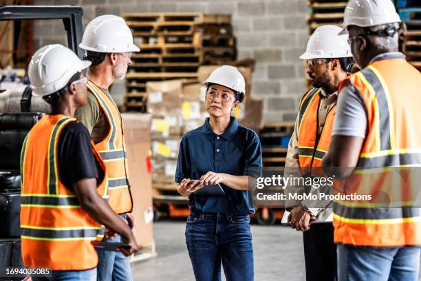 female warehouse supervisor speaking with a group of employees - seguridad y salud ocupacional fotografías e imágenes de stock