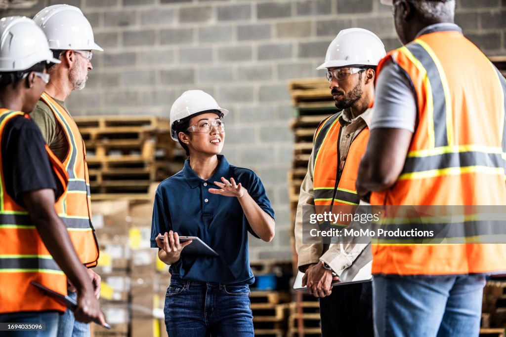 Female warehouse supervisor speaking with a group of employees