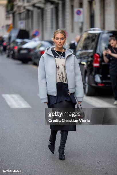 Emili Sindlev wears blue hooded jacket, shirt with print in navy, silver Alaia bag, skirt, laced boots, necklace outside Max Mara during the Milan...