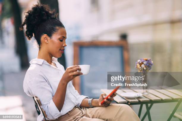 a happy beautiful cuban businesswoman texting on her mobile phone while enjoying drinking coffee at the cafe - applications stock pictures, royalty-free photos & images