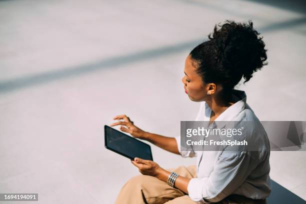 a beautiful cuban businesswoman watching something on her tablet while relaxing outdoors - thinking cap stock pictures, royalty-free photos & images