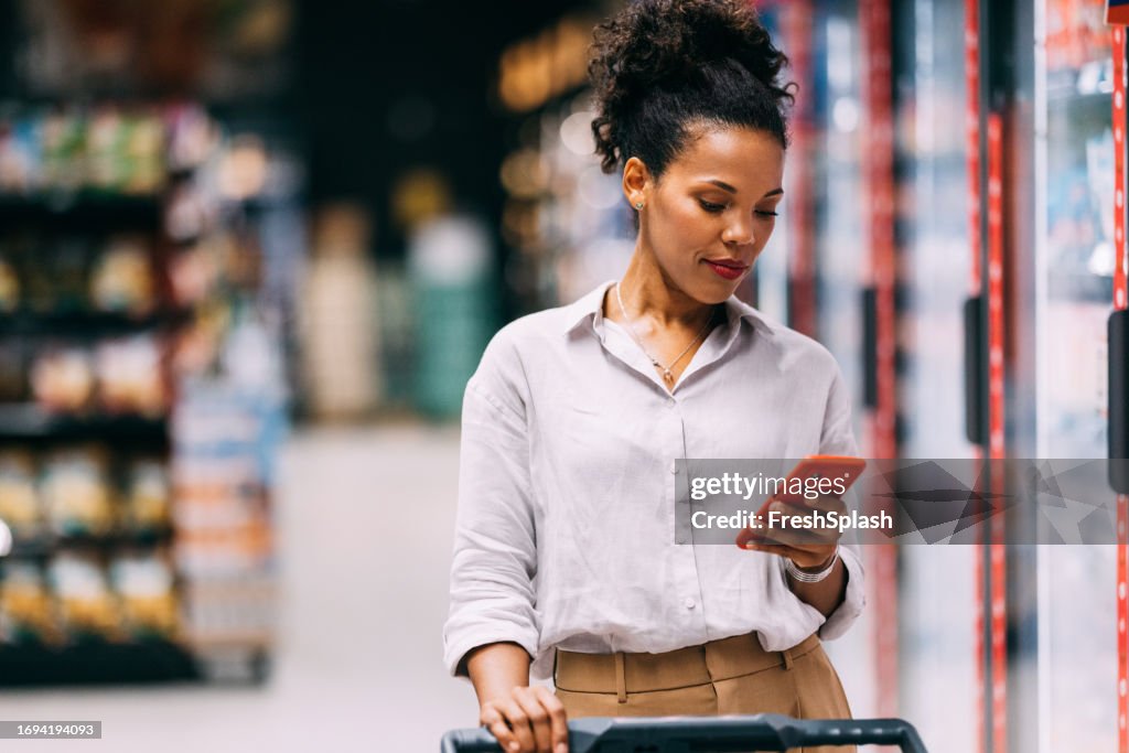 A Happy Beautiful Cuban Woman Texting On Her Mobile Phone While Shopping At The Supermarket