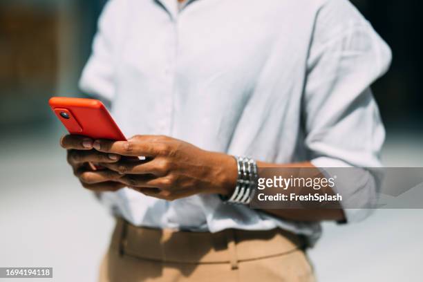 uma bela empresária cubana irreconhecível enviando mensagens de texto em seu celular - camisa cor de laranja - fotografias e filmes do acervo