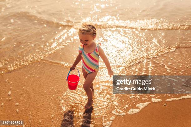 happy little girl running at shoreline at the beach. - sand castle stock pictures, royalty-free photos & images