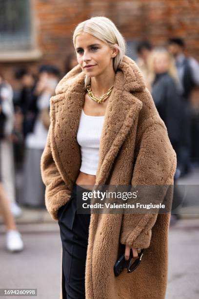 Caro Daur is seen wearing Max Mara brown sunglasses, a gold chain necklace, a white belly-off tank top, a teddy long beige coat and low waist black...