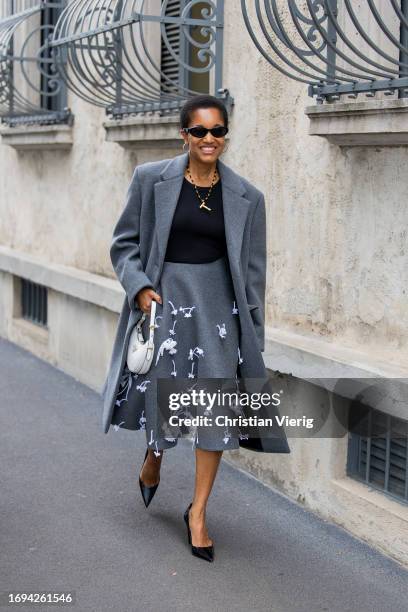 Tamu McPherson wears grey high waisted skirt, coat, white bag outside Prada during the Milan Fashion Week - Womenswear Spring/Summer 2024 on...