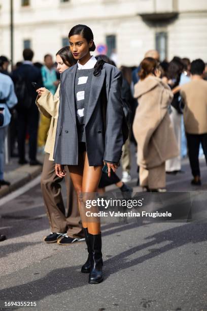 Model is seen wearing black leather boots, an oversized grey blazer, a white shirt and a striped grey and white sweater outside the Max Mara show...