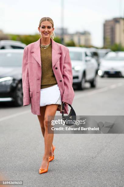 Emili Sindlev wears a golden necklace, a pink oversized blazer jacket, a khaki wool pullover, a white mini skirt, orange Prada pointed shoes, a black...