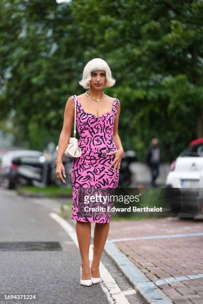 Bettina Looney wears a golden chain necklace, a low-neck pink and black dress with printed patterns, a white bag, white pumps / pointed shoes,...