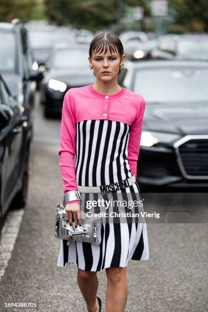 Courtney Mawhorr wears black white striped dress with belt, silver bag, pink cropped cardigan outside Moschino during the Milan Fashion Week -...