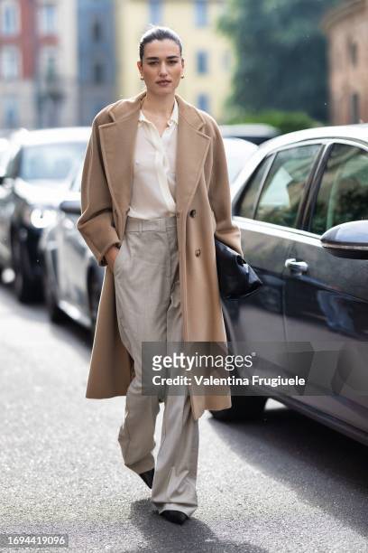 Ilirida Krasniqi is seen wearing gold earring, a white cream shirt, a long beige coat and wide leg high waist beige trousers outside the Max Mara...