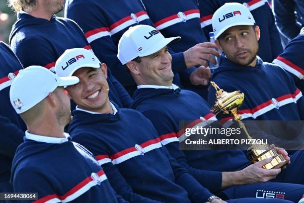 Captain, Zach Johnson holding the trophy, smiles as sits beside US golfer, Xander Schauffele and US golfer, Collin Morikawa at the US team official...