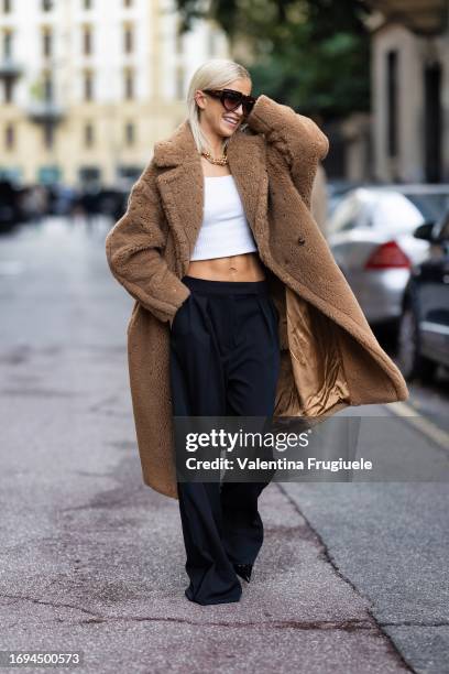 Caro Daur is seen wearing Max Mara brown sunglasses, a gold chain necklace, a white belly-off tank top, a teddy-bear long beige coat and low waist...