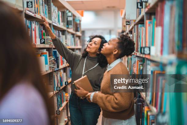 hispanic student searching for a book with a librarian - librarian bildbanksfoton och bilder
