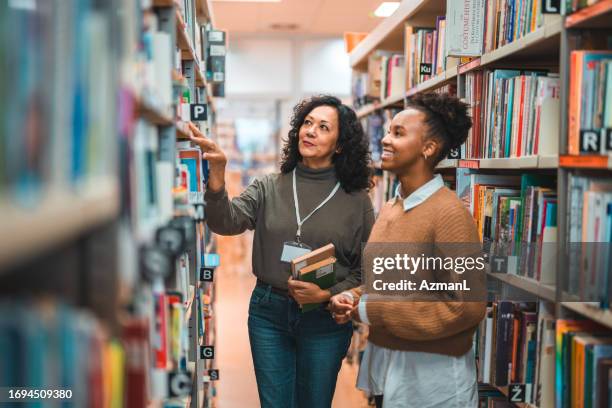 mid adult hispanic librarian escorting a student in a library - bibliotek bildbanksfoton och bilder
