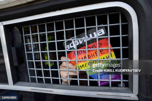 Russian gay and LGBT rights activist shows sign reading "Love is stronger than homophobia" from inside of a Russian riot police van during...