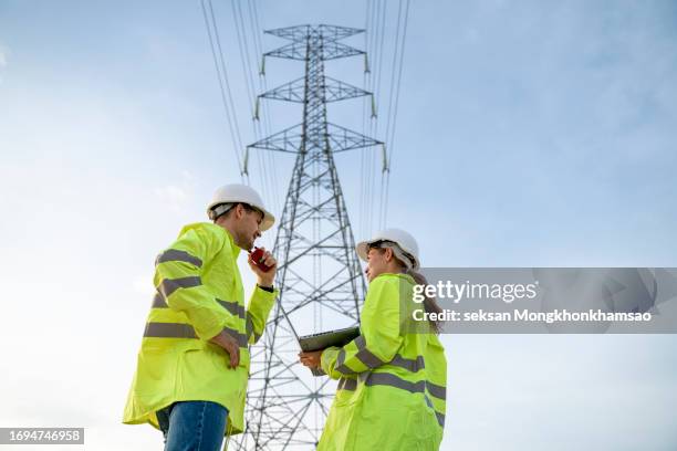 team of electricians is working on a plan to fix a high-voltage transmission line problem by looking at information received from problem reports on a laptop computer. - pylone-electrique photos et images de collection