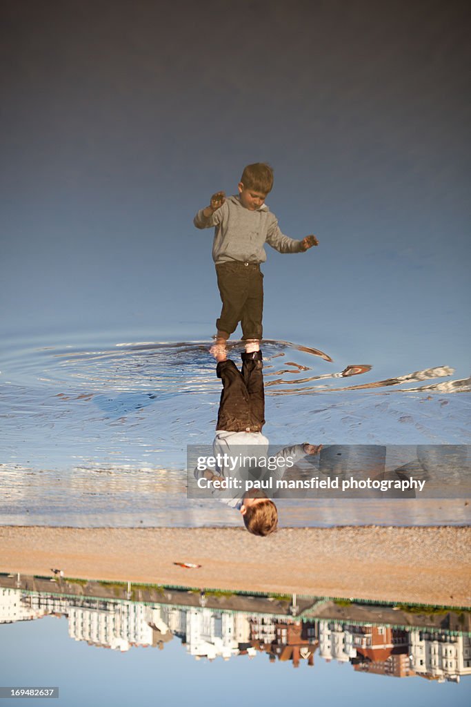 Boy reflected in puddle on Brighton beach