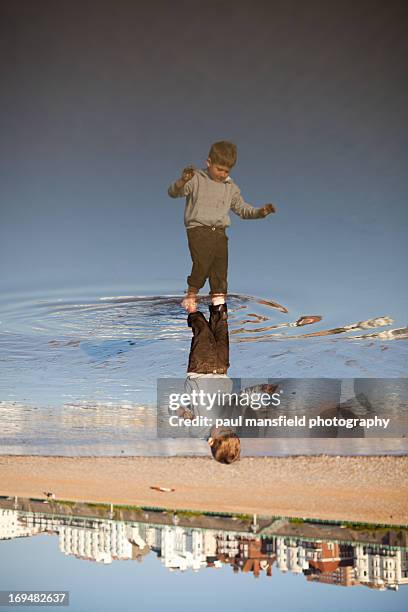 boy reflected in puddle on brighton beach - puddle stock pictures, royalty-free photos & images
