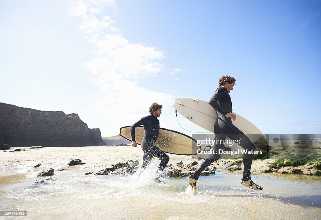 Surfers running along beach.