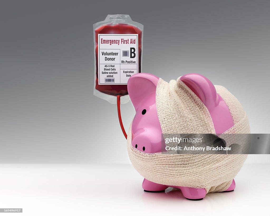Bandaged pink piggy bank receiving a transfusion