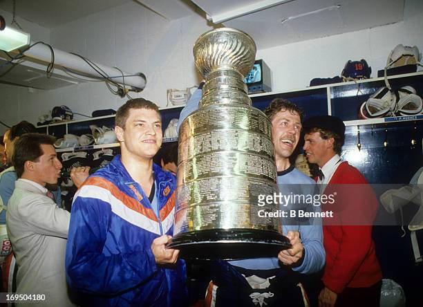 Esa Tikkanen and Willy Lindstrom of the Edmonton Oilers celebrate with the Stanley Cup Trophy in the locker room after the Oilers defeated the...