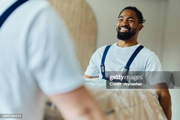 glücklicher schwarzer beweger, der mit möbeln in der wohnung arbeitet. - möbelpacker stock-fotos und bilder