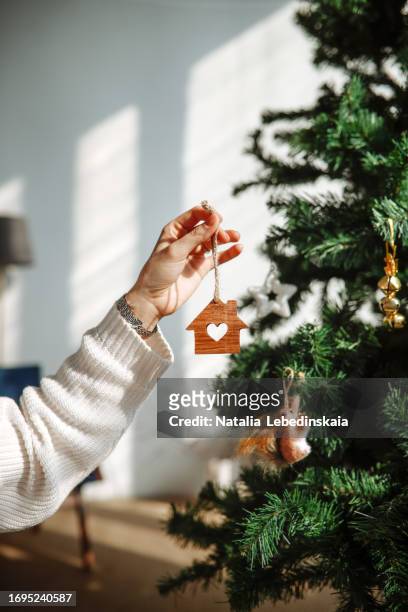 woman holds wooden house with heart window near christmas tree, eco-friendly decor - homeowners decorate their houses for christmas stockfoto's en -beelden