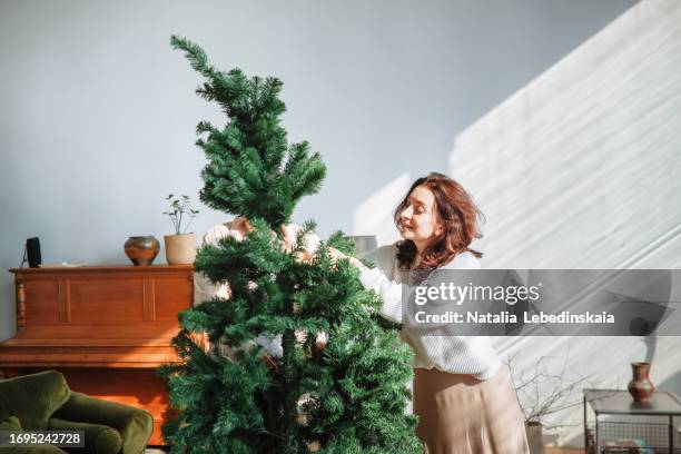 beautiful brunette in cozy sweater is assembling christmas tree from several parts, - posicionamiento fotografías e imágenes de stock