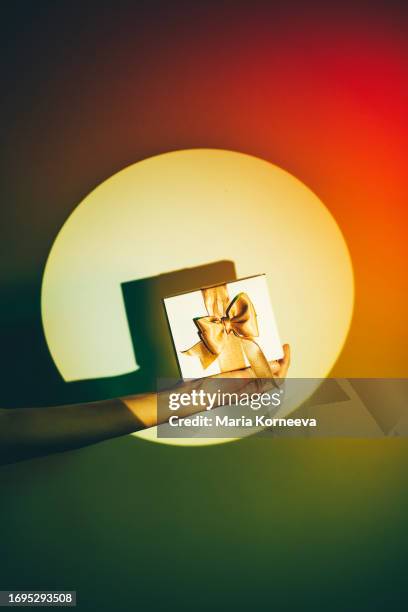 woman's hand holding a christmas gift on a colorful background. - exchanging gifts stock pictures, royalty-free photos & images