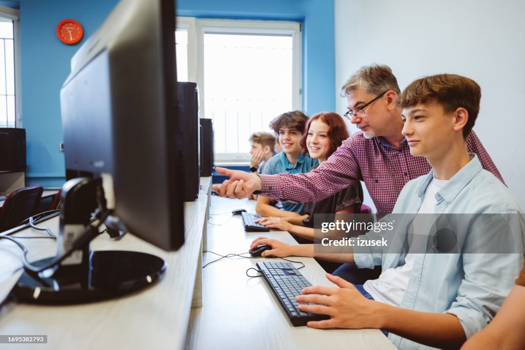 High school students talking with male teacher during programming lessons