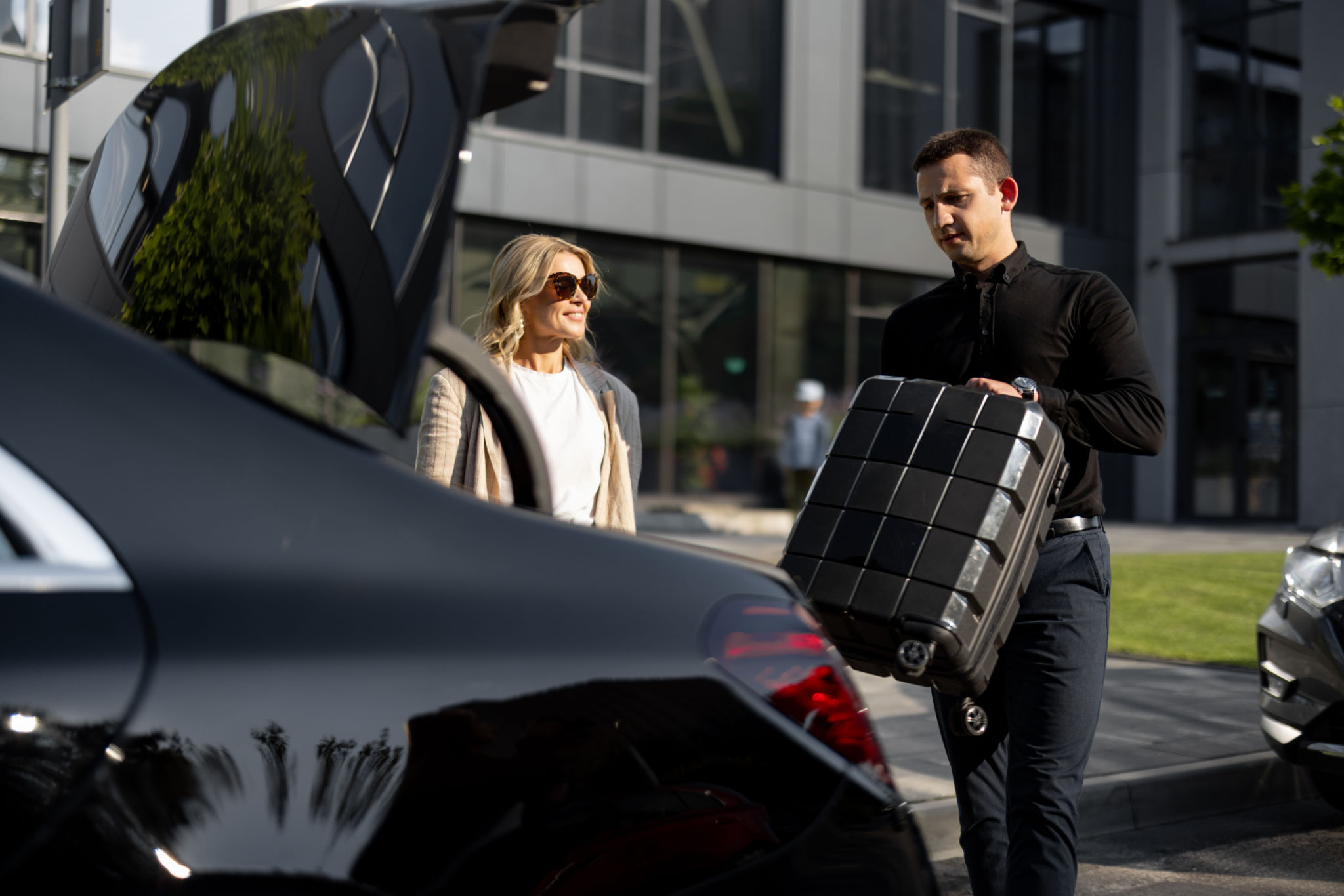 Businesswoman waits while chauffeur packs a suitcase in car trunk Businesswoman waits while chauffeur packs a suitcase in car trunk
