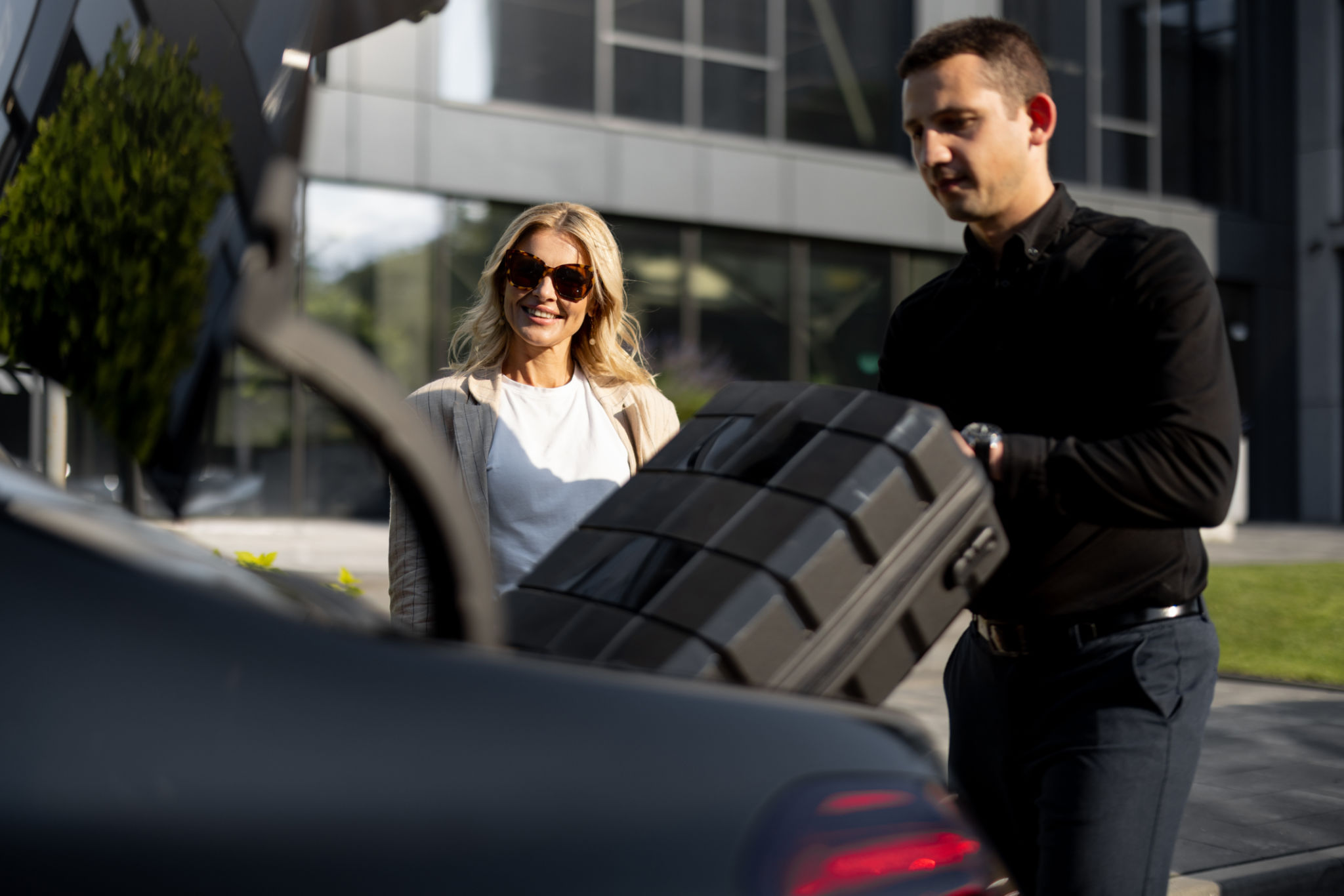 Businesswoman waits while chauffeur packs a suitcase in car trunk Businesswoman waits while chauffeur packs a suitcase in car trunk